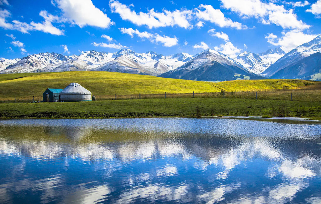 Alpine lake, grassland and yurt beneath snow-capped mountains in Xinjiang