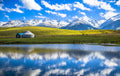 Alpine lake, grassland and yurt beneath snow-capped mountains in Xinjiang