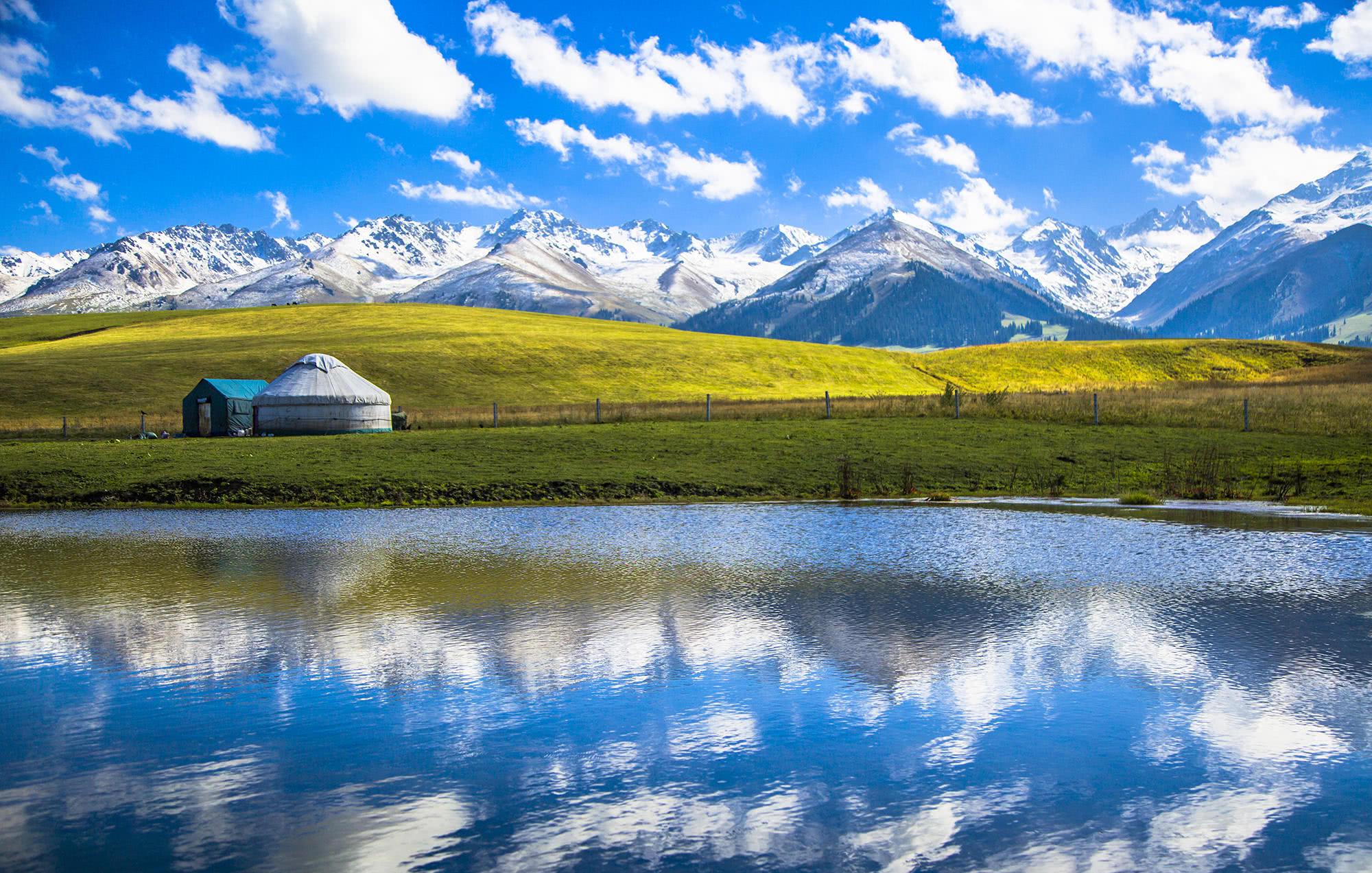 Alpine lake, grassland and yurt beneath snow-capped mountains in Xinjiang