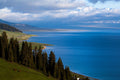Blue Sayram Lake with forested slopes and snow-capped mountains in Xinjiang